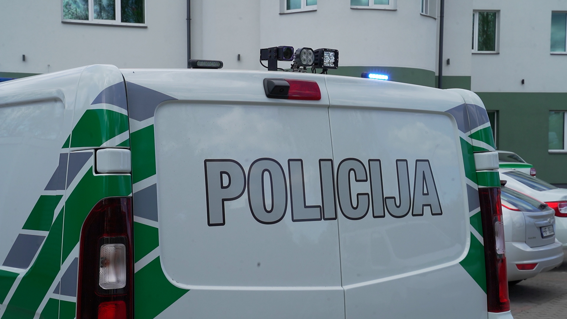 Pašvaldības policijas busiņš ar ieslēgtu bākuguni stāv pie ēkas