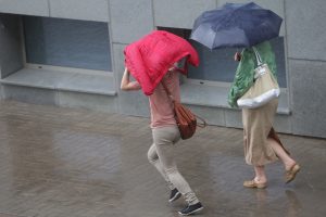 Sievietes lietū ar lietussargu un jaku virs galvas pilsētas ielā