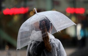 Cilvēks lietū ar caurspīdīgu lietussargu un lietusmēteli