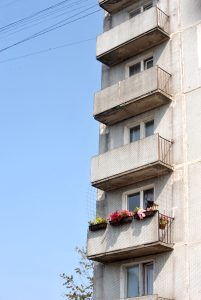 Vecs daudzdzīvokļu mājas balkons ar puķu podiem otrajā stāvā.