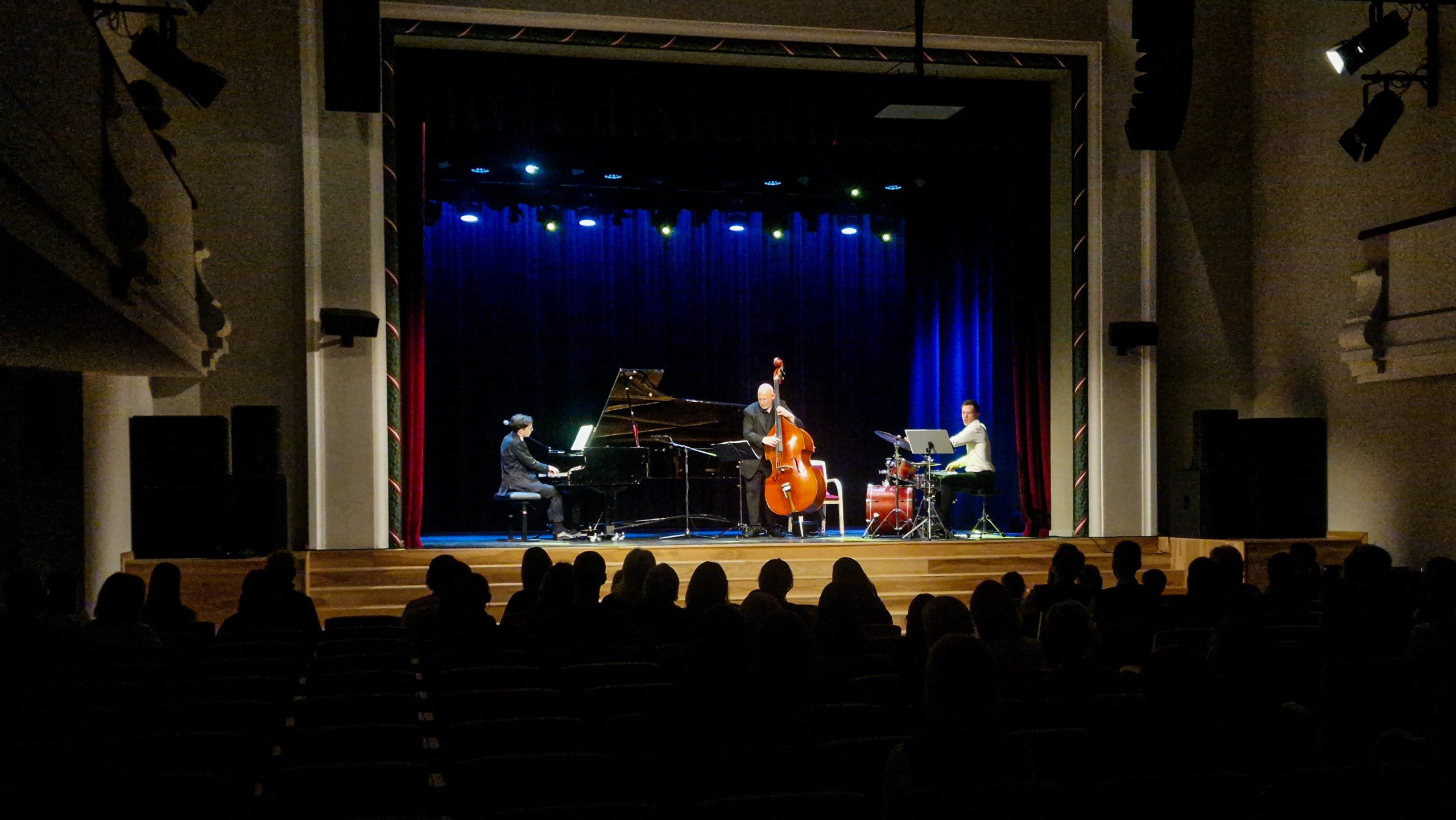 Koncerts uz skatuves, kur muzicē pianists, kontrabasists un sitaminstrumentālists.