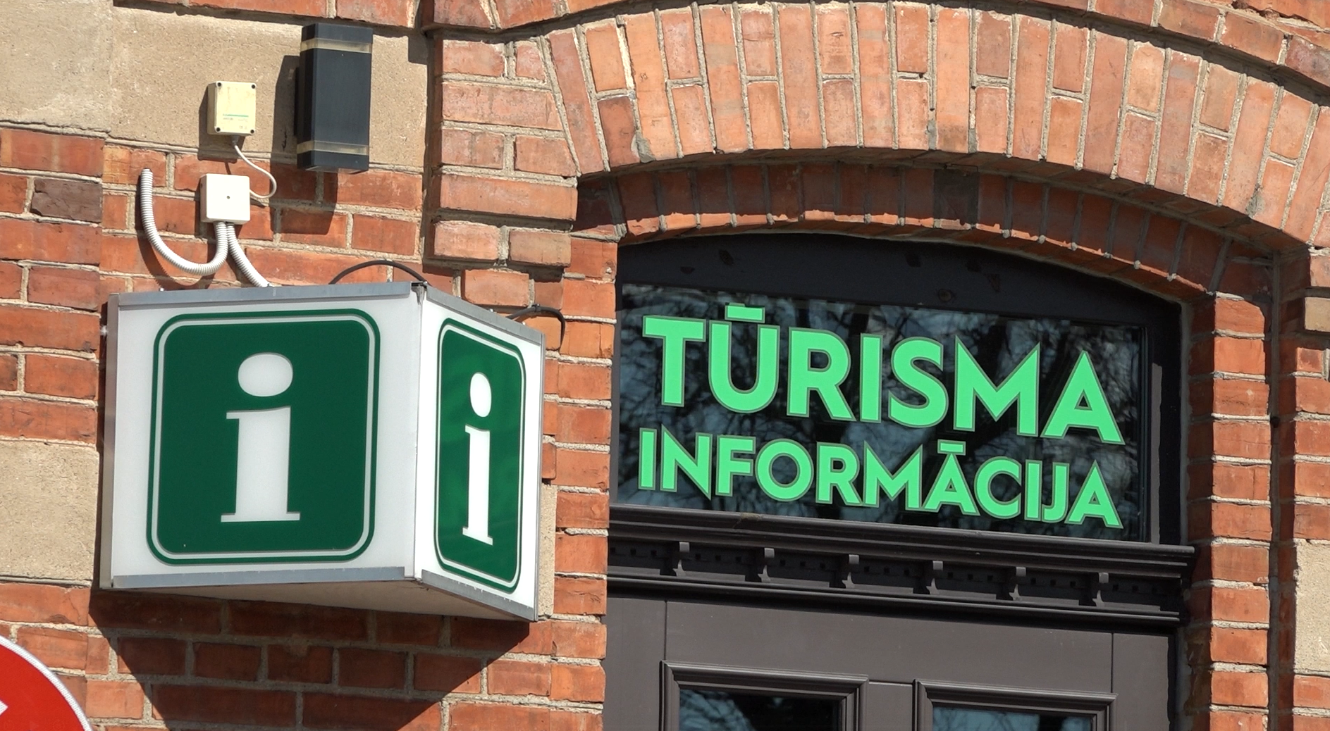 Tūrisma informācijas centra izkārtne uz ķieģeļu ēkas fasādes.