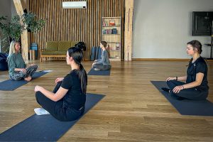 Sievietes jogas nodarbībā sēž meditācijas pozā uz paklājiņiem modernā studijā
