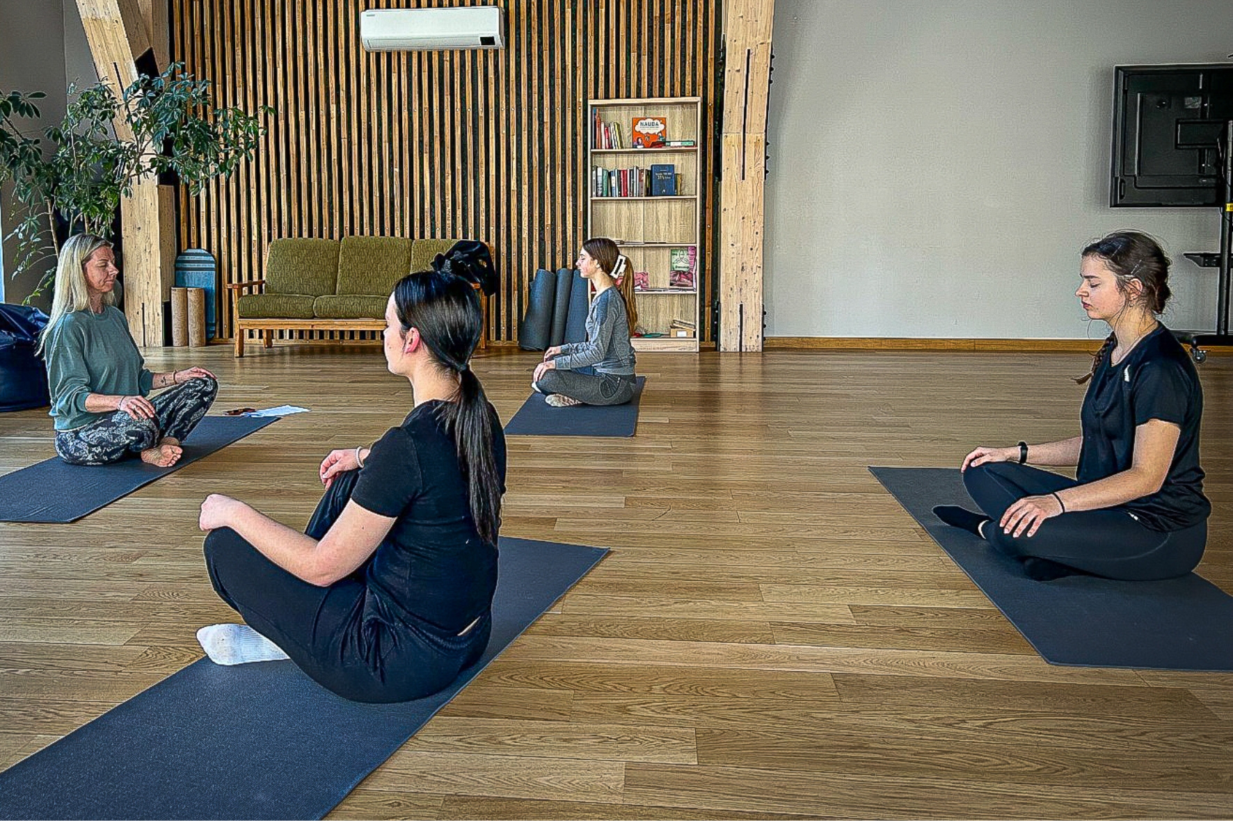 Sievietes jogas nodarbībā sēž meditācijas pozā uz paklājiņiem modernā studijā
