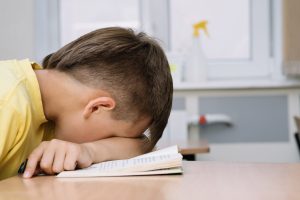 Noguris zēns ar galvu uz grāmatas klasē