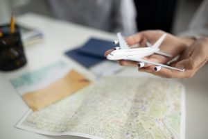 Rokās turēts rotaļlidmašīnas modelis virs kartes un ceļojuma dokumentiem.