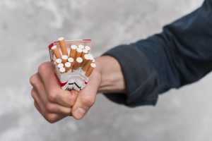 Saspiesta cigarešu paciņa vīrieša rokā.