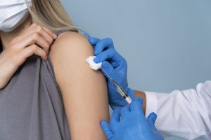 Sieviete saņem vakcīnu plecā, medicīniskajam personālam valkājot cimdus