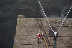 Makšķere un uztveramais tīkls uz koka laipas pie ūdens