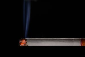 Degoša cigarete ar dūmiem uz melna fona