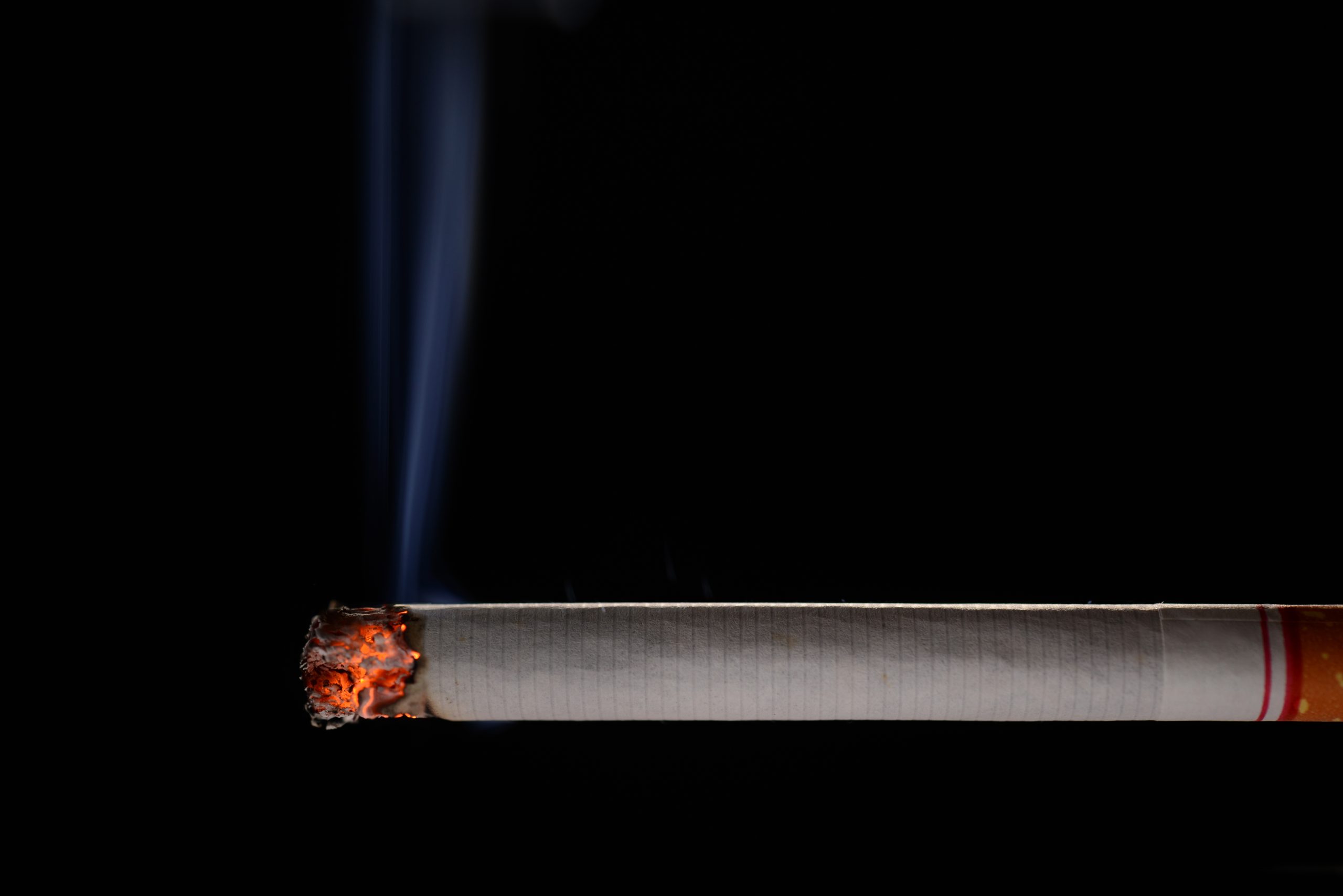 Degoša cigarete ar dūmiem uz melna fona