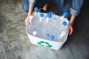 Cilvēks tur pārstrādei paredzētu konteineru ar tukšām plastmasas pudelēm