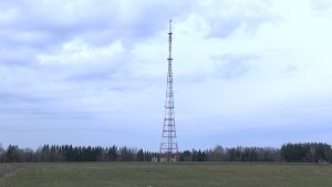 Radio un televīzijas tornis atklātā laukā ar meža fonu