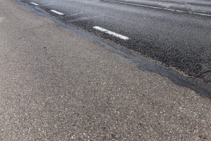 Ceļš ar baltām ceļa zīmēm un slapju virsmu.