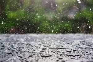 Lietus lāses krīt uz virsmas ar izplūdušu zaļu fonu pavasarī