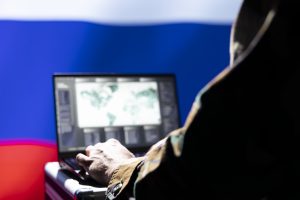 Persona militārā tērpā analizē datus datorā Krievijas karoga fonā