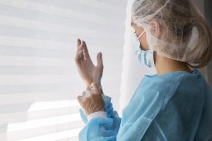 Medicīnas darbiniece uzvelk cimdus, valkājot aizsargapģērbu