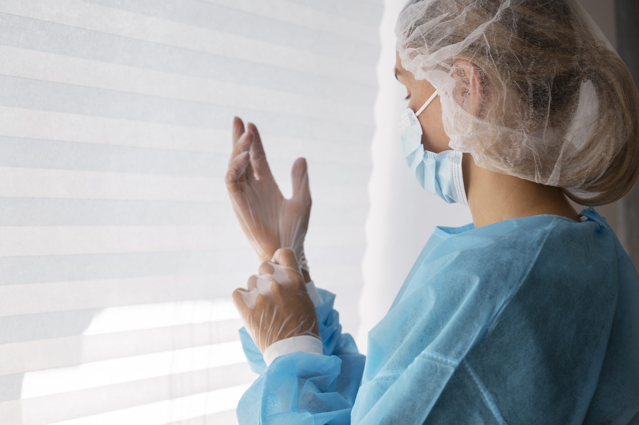 Medicīnas darbiniece uzvelk cimdus, valkājot aizsargapģērbu