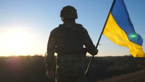 Ukrainas karavīrs ar karogu saulrietā