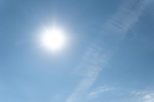 Spoža saule zilās debesīs ar plāniem mākoņiem