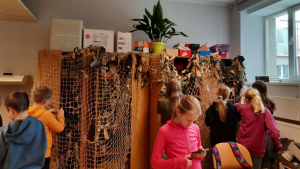 Skolēni darina maskēšanās tīklu Ukrainas aizstāvjiem klasē.