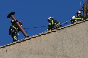 ugunsdzēsēji uz jumta ar drošības virvēm un metāla cauruli