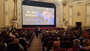 Kinoteātra ekrāns ar dokumentālās filmas "Mēs, mūsu mājdzīvnieki un karš" plakātu