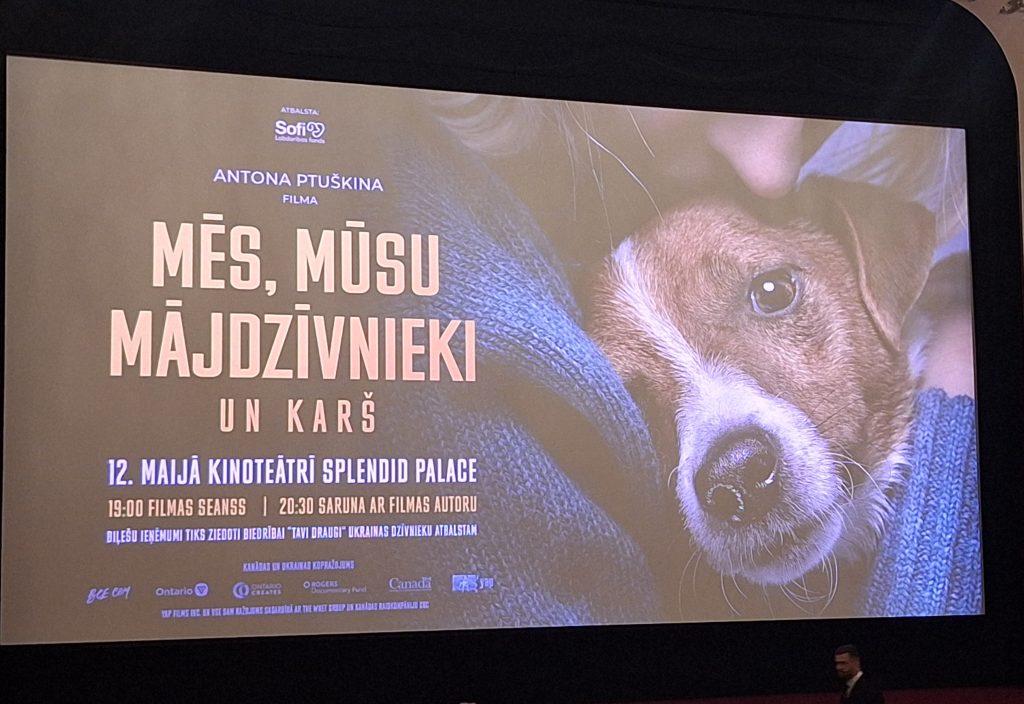 Kinoteātra ekrāns ar dokumentālās filmas "Mēs, mūsu mājdzīvnieki un karš" plakātu