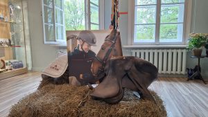 Jātnieka ekspozīcija ar seglu, fotogrāfiju un uzrakstu “Latvija”