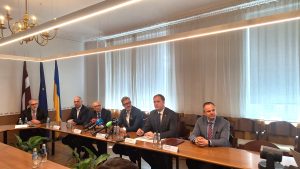Vairāki vīrieši, tostarp Ekonomikas ministrs Viktors Valainis, sēž pie gara galda memoranda parakstīšanas brīdī