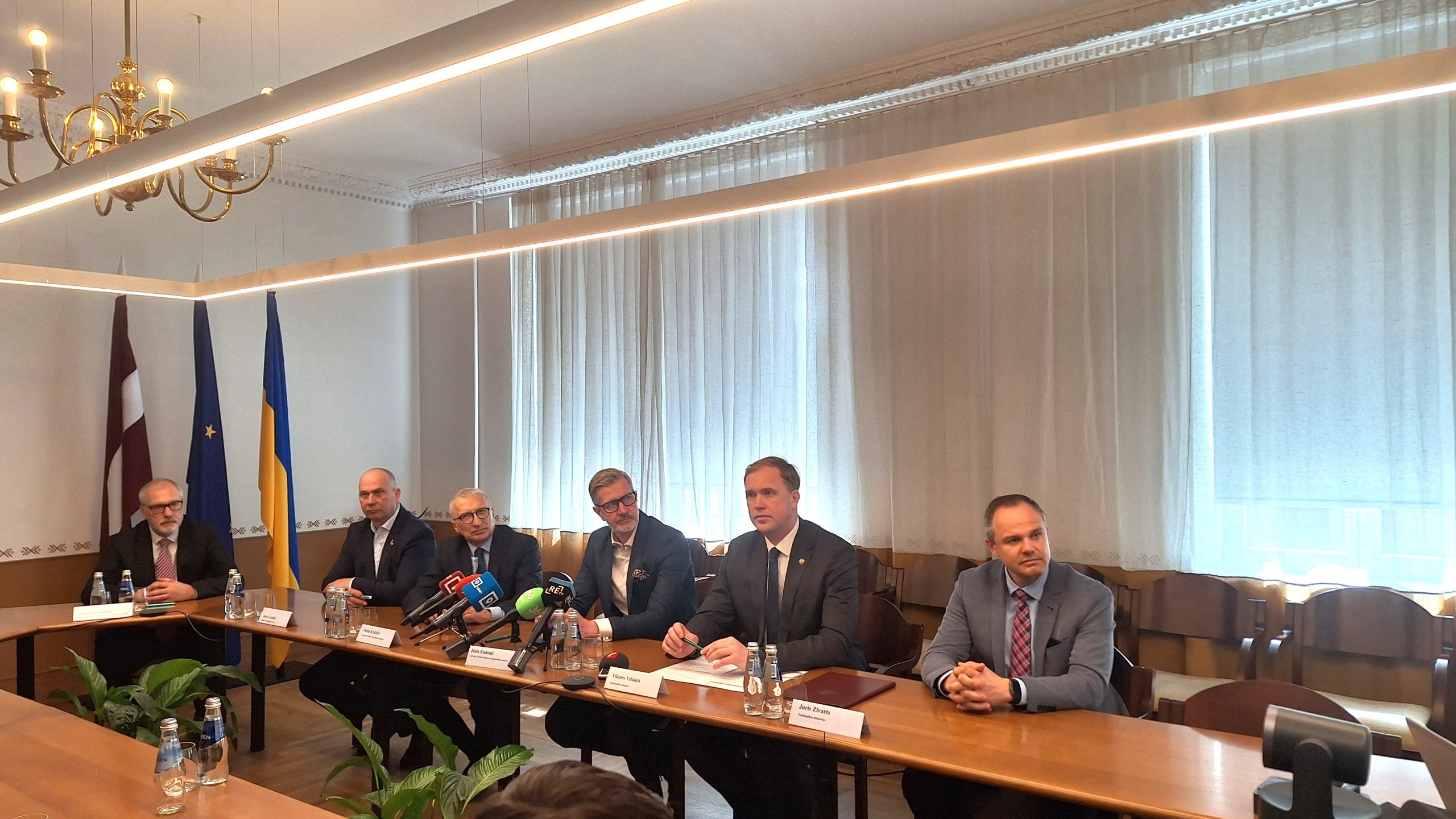 Vairāki vīrieši, tostarp Ekonomikas ministrs Viktors Valainis, sēž pie gara galda memoranda parakstīšanas brīdī