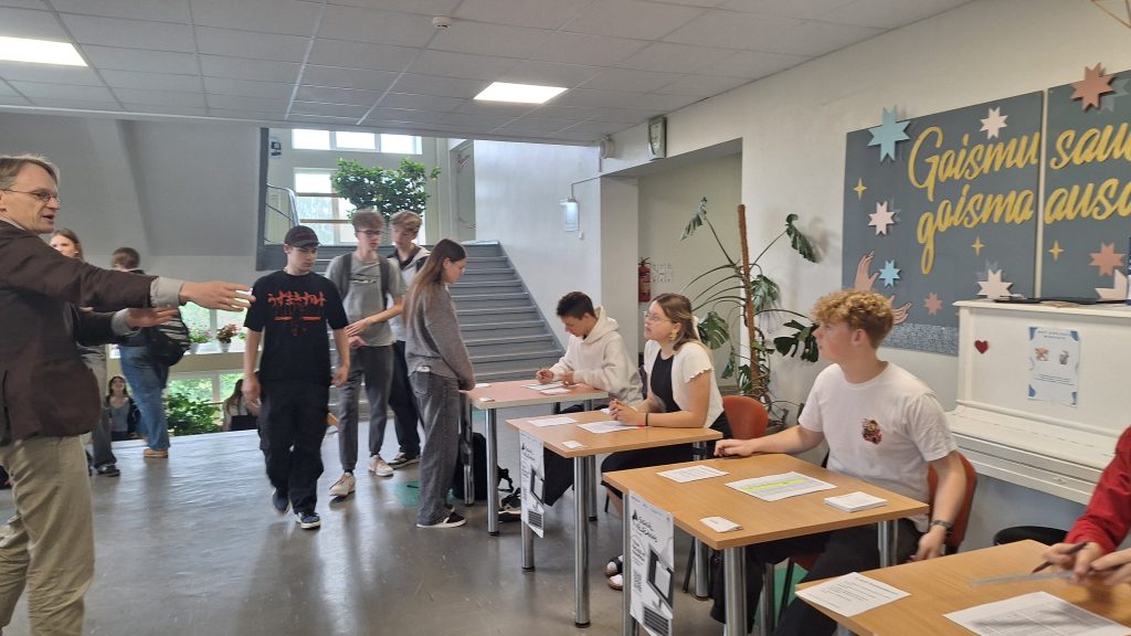 Skolēni un pieaugušais vēlēšanu norises vietā Jelgavas Spīdolas Valsts ģimnāzijā