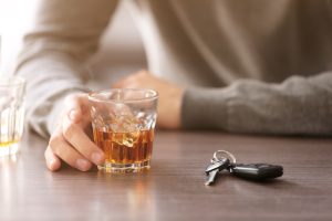 Roka tur glāzi ar viskiju, blakus uz galda atrodas automašīnas atslēgas