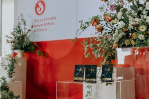 Nikolaja Pakalniņa balvas uz stikla pjedestāla ar Bērnu slimnīcas logotipu un ziedu dekorācijām fonā.