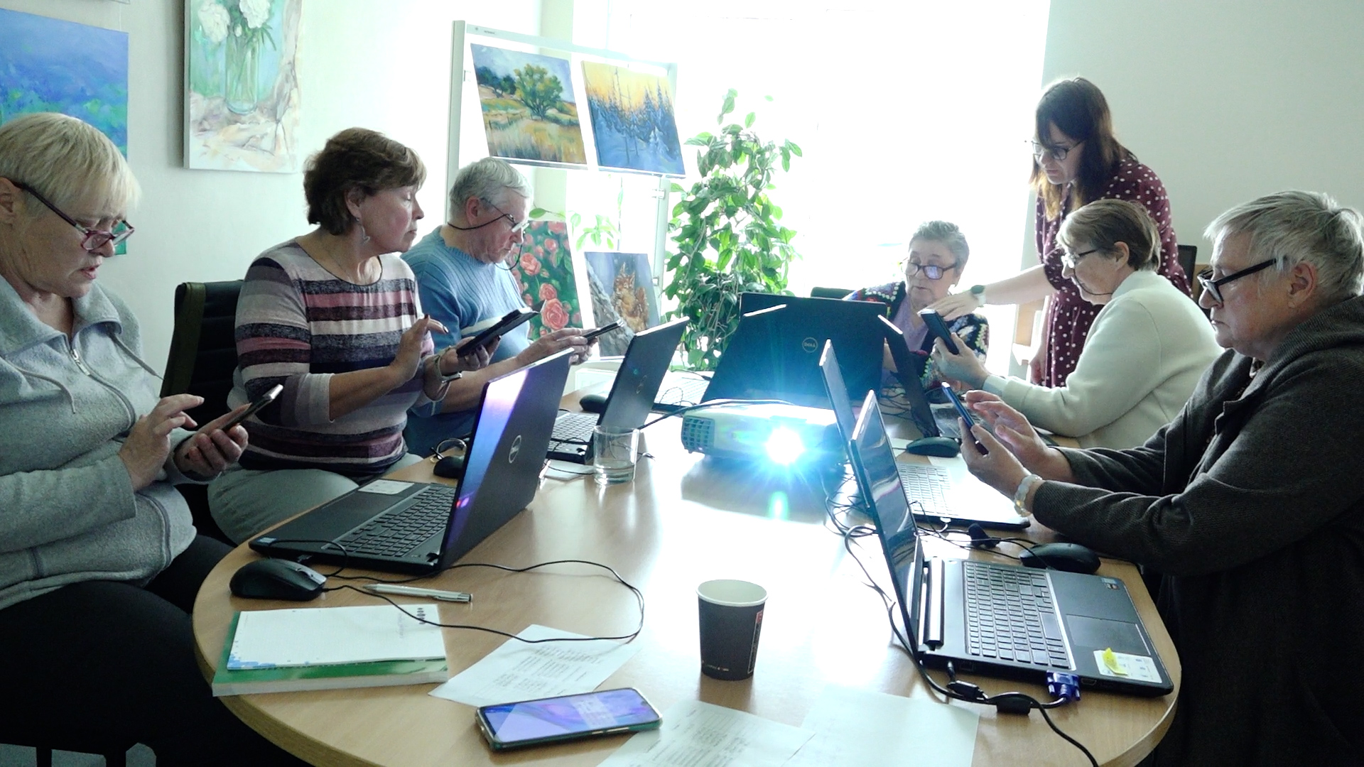 Seniori mācās izmantot viedtālruņus un datorus digitālo prasmju nodarbībā bibliotēkā