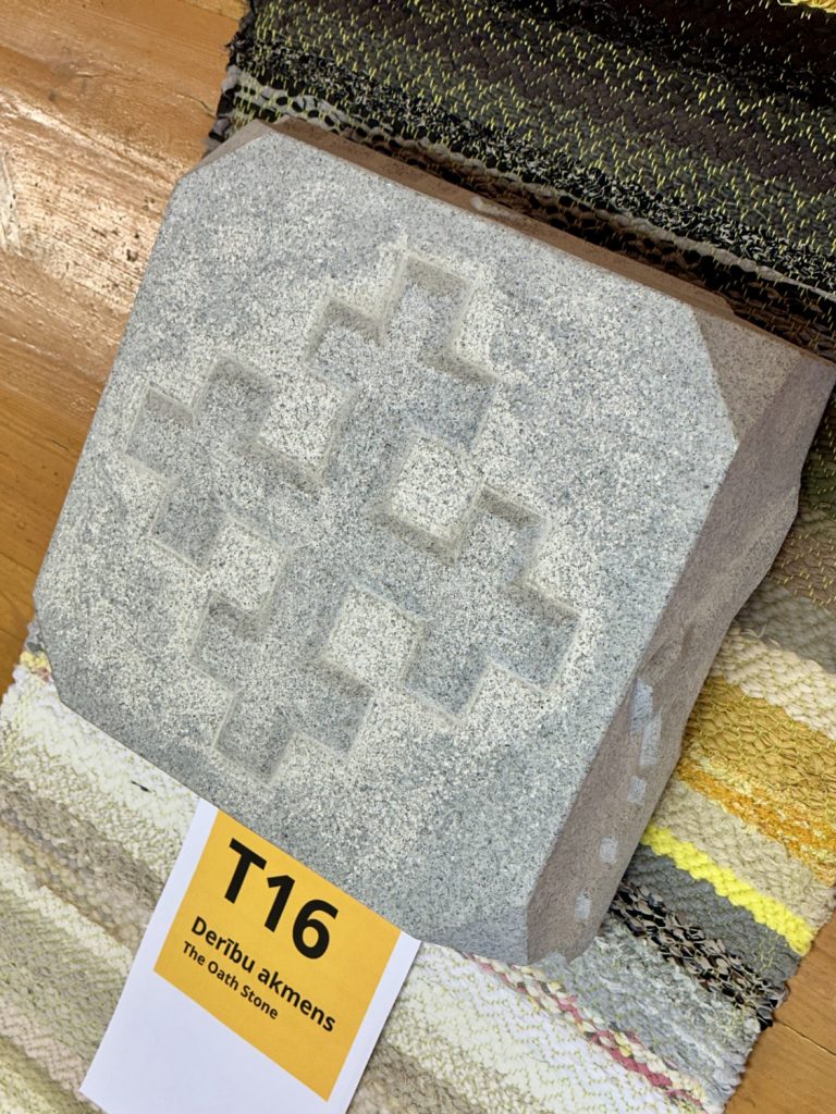 Liels, pelēks akmens ar iekaltu krustveida simbolu, novietots uz rakstaina auduma
