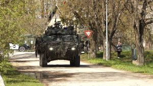 Maskēts militārais transportlīdzeklis brauc pa ceļu apdzīvotā vietā mācību laikā.