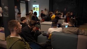 Grupa studentu klausās prezentāciju vai lekciju telpā ar projekcijas ekrānu Ventspilī