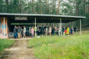 Cilvēki pulcējas zem "INČUPE" dzelzceļa pieturas nojumes lietainā laikā meža ielokā Saulkrastos