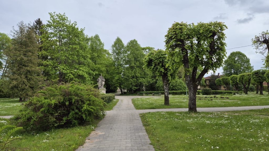 Ainavisks skats uz 1905. gada parku Kuldīgā ar plašiem zaļumiem, kokiem un pieminekli, kas norāda uz parka kultūrvēsturisko nozīmi