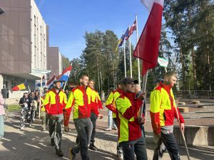 Jaunieši krāsainos formas tērpos soļo ar nacionālajiem karogiem starptautiskā pasākumā