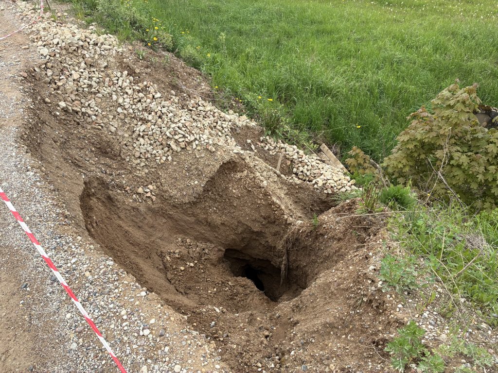 Liels zemes iegruvums grants ceļa malā, ko ieskauj nožogojuma lente