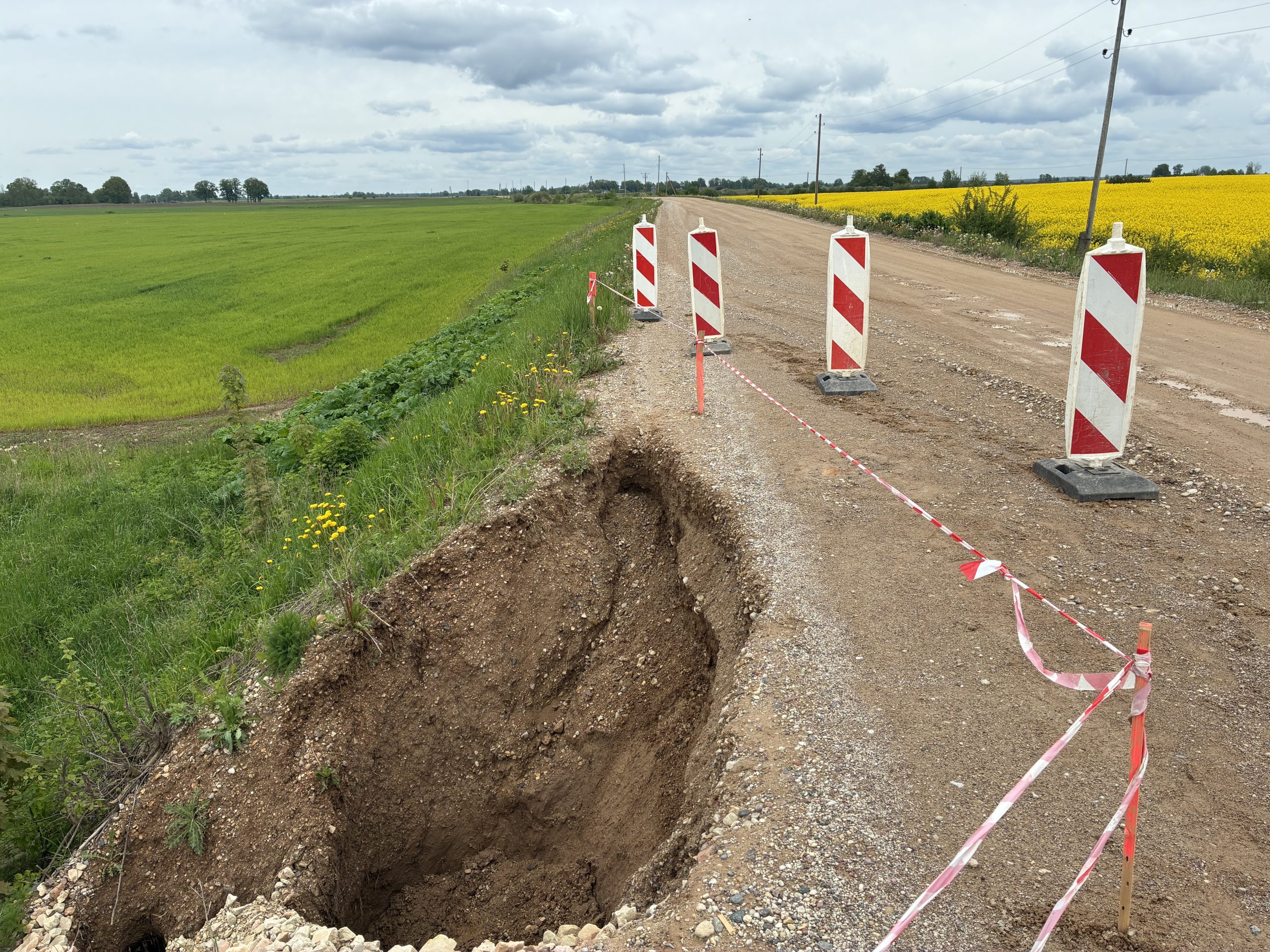 Grants ceļa posms ar zemes iegruvumu malā, nožogots ar brīdinājuma lentām un ceļa zīmēm