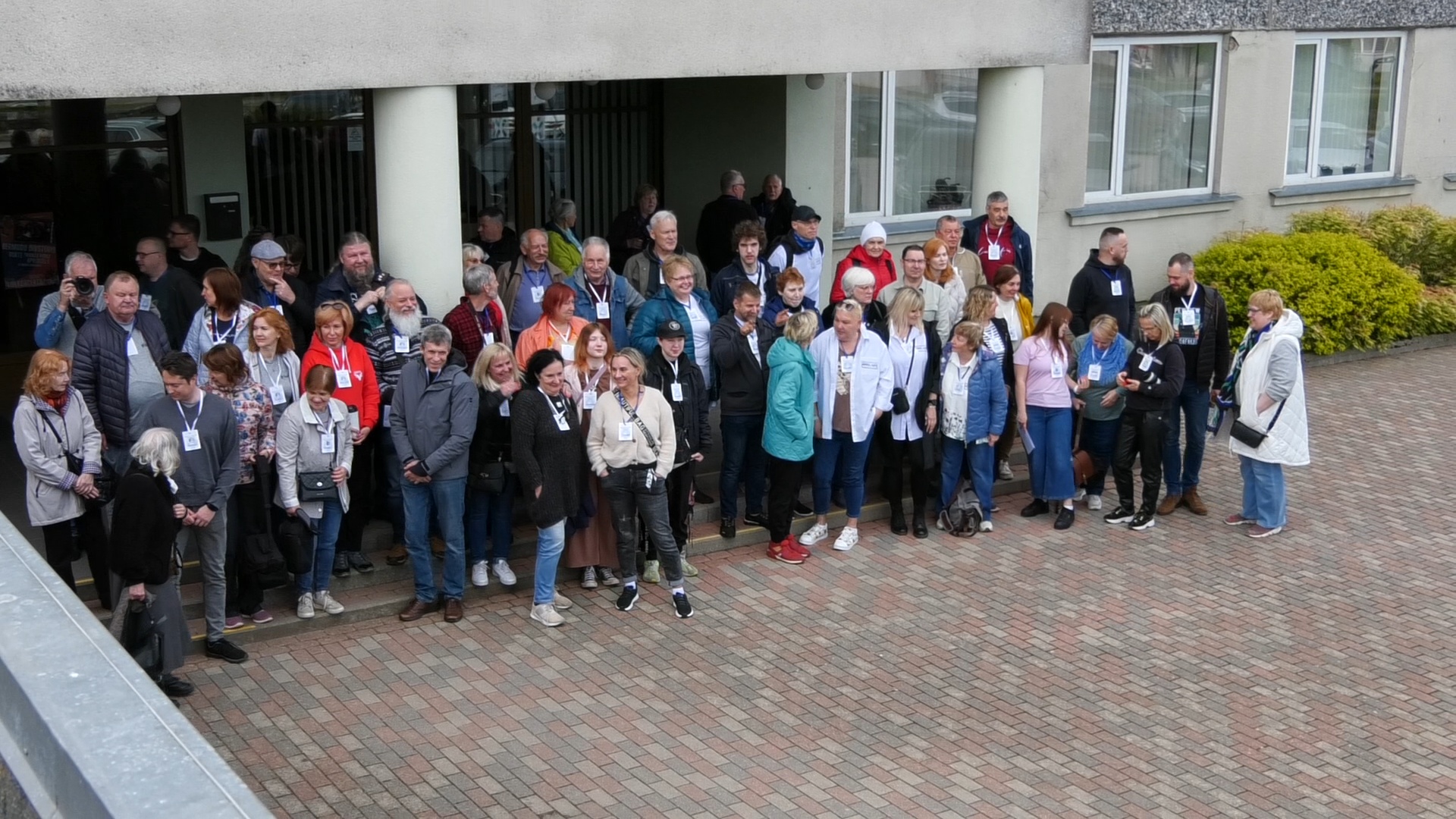 Liela grupa cilvēku, kas piedalās Kurzemes fotodienās, stāv pie ēkas ieejas