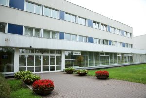 Latvijas Onkoloģijas centra ēka ar stiklotu ieeju un ziedošiem puķu podiem priekšā