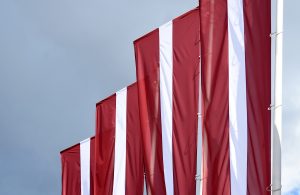 Latvijas karogi plīvo vējā uz pelēka debesu fona