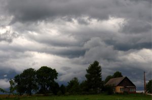 Tumši lietus mākoņi virs lauku mājas un kokiem
