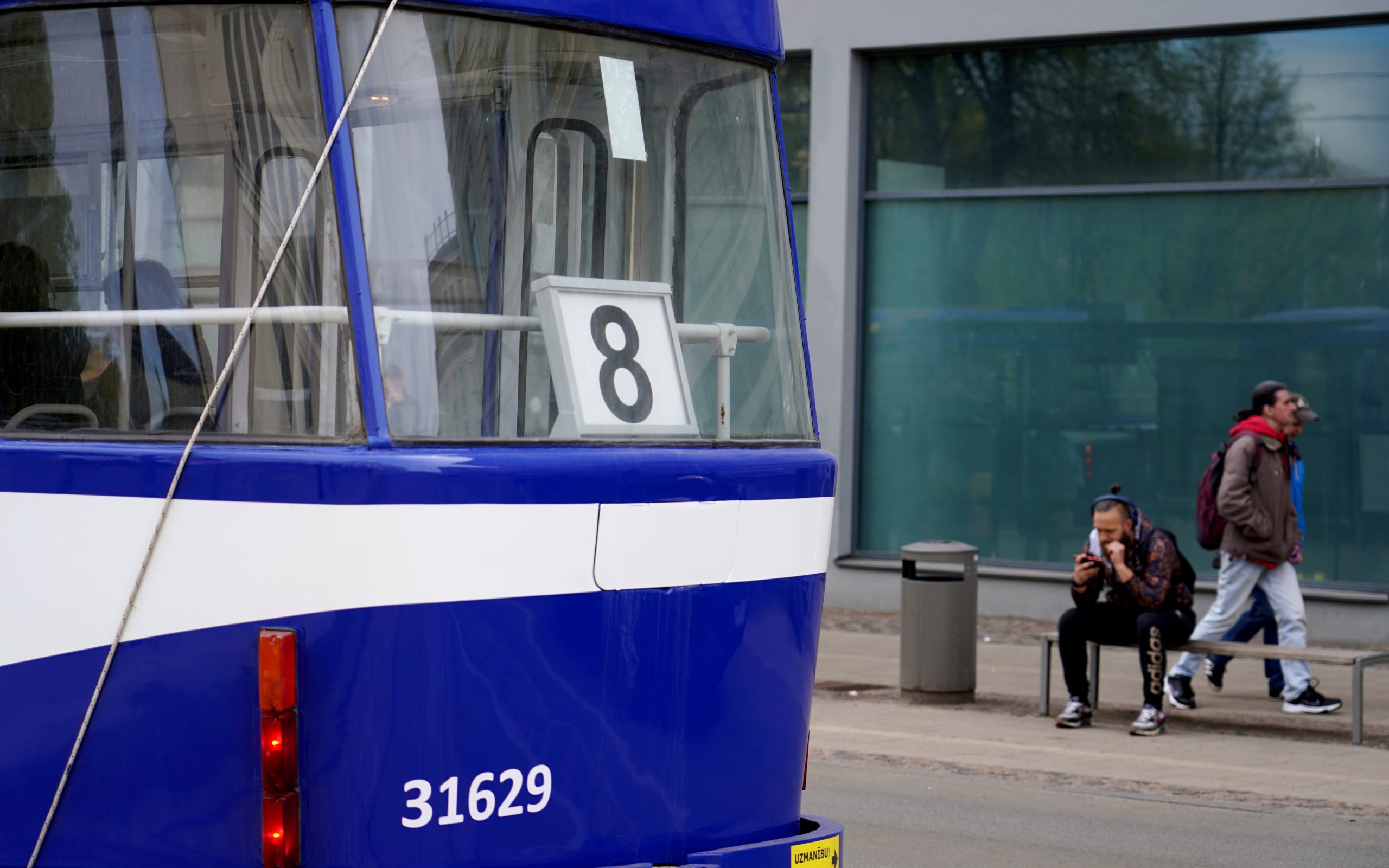 Zils 8. maršruta tramvajs pieturā ar pasažieriem fonā