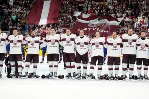 Latvijas hokeja izlase stāv plecu pie pleca pirms spēles ar fanu karogiem fonā