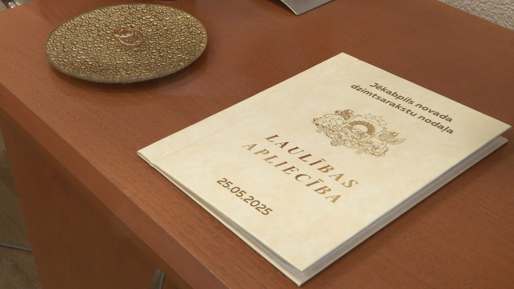 Tuvplāns ar laulības apliecību, uz kuras redzams uzraksts "LAULĪBAS APLIECĪBA" un datums "25.05.2025"